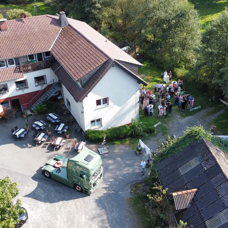 Feierliche Veranstaltung in der Pension Mausmühle Luftaufnahme einer Feier in der Pension Mausmühle mit Gästen im Gartenbereich und dekorierten Sitzplätzen im Hof.